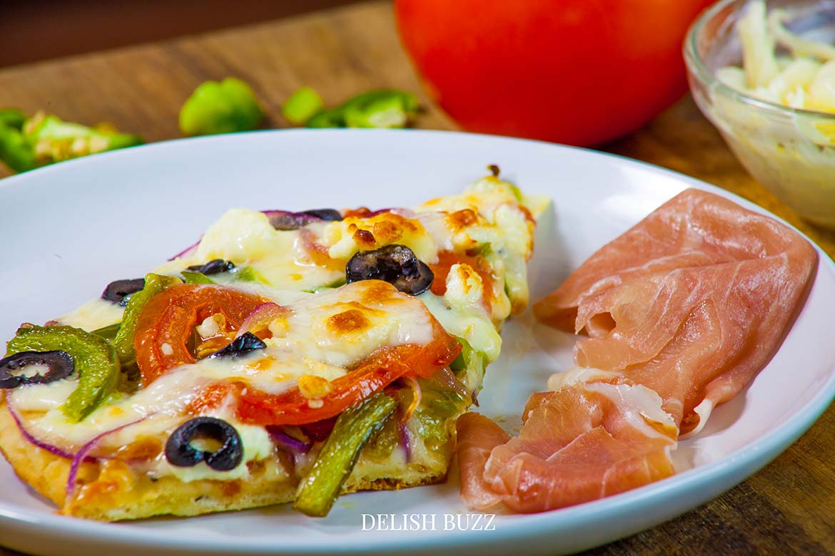 Light but extremely delicuious artisan homemade flatbread pizza. A robust Greek pizza, full of fresh crispy flavors. Satisfying naan bread pizza with perfectly melted cheeses. Perfect meal for a busy day. Prepped and ready to eat in minutes. - www.delishbuzz.com